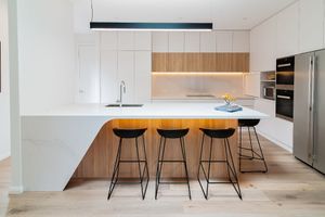 Sleek modern kitchen with white cabinets, wooden accents and black bar stools at island counter.