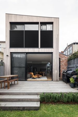 Contemporary two-story house with vertical timber cladding and large glass sliding doors opening to deck.