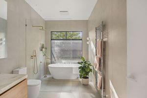 Modern bathroom with freestanding tub under window, beige walls and heated towel rail.