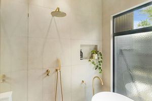 Light-filled bathroom with brass fixtures, freestanding tub and indoor plants near window.