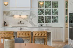 Elegant dining area with marble backsplash and wooden chairs near large windows.