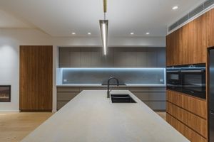 Sleek modern kitchen with wooden cabinets, white countertops and linear pendant lighting.