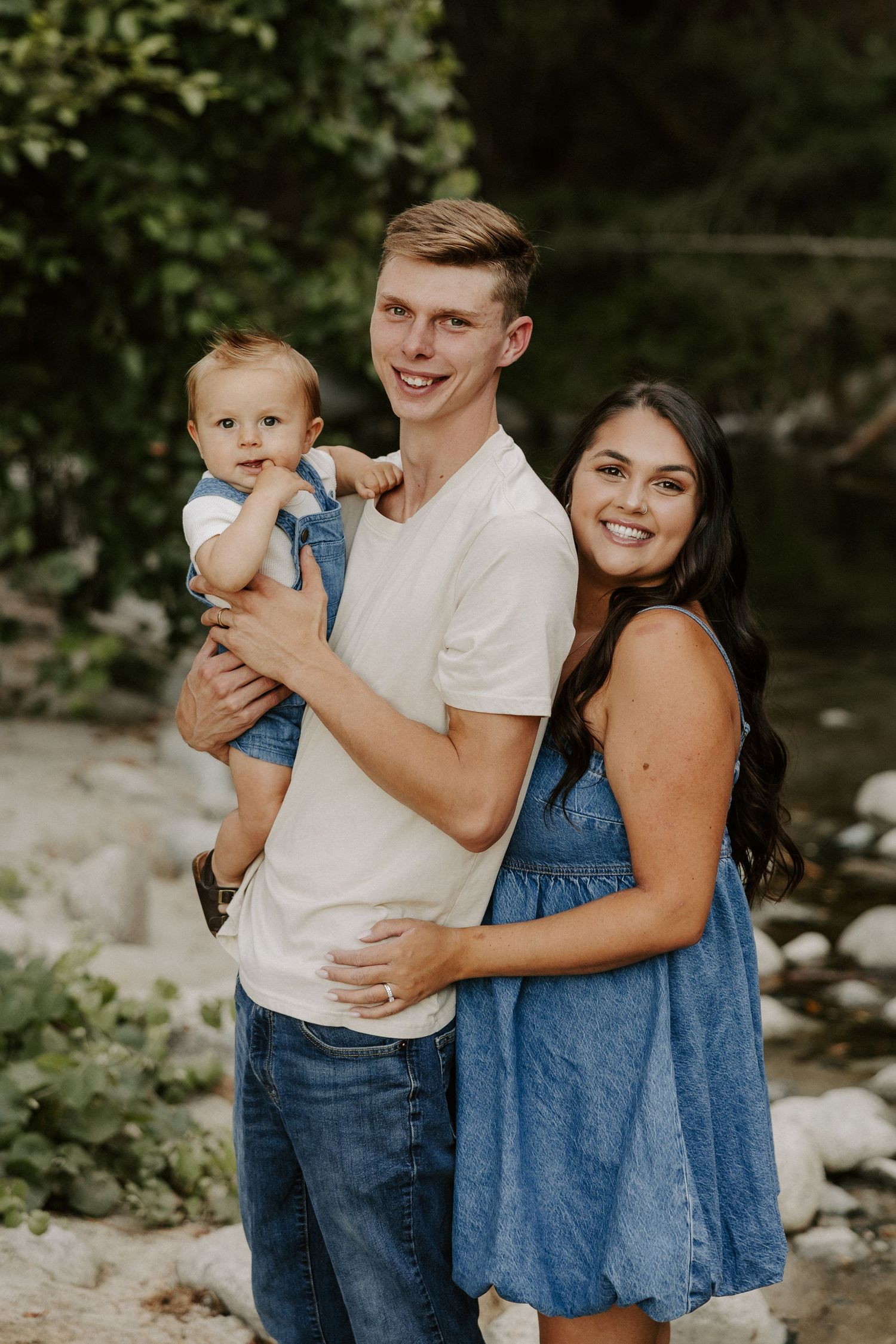 A family poses together outdoors in coordinated denim and white outfits against a natural backdrop.