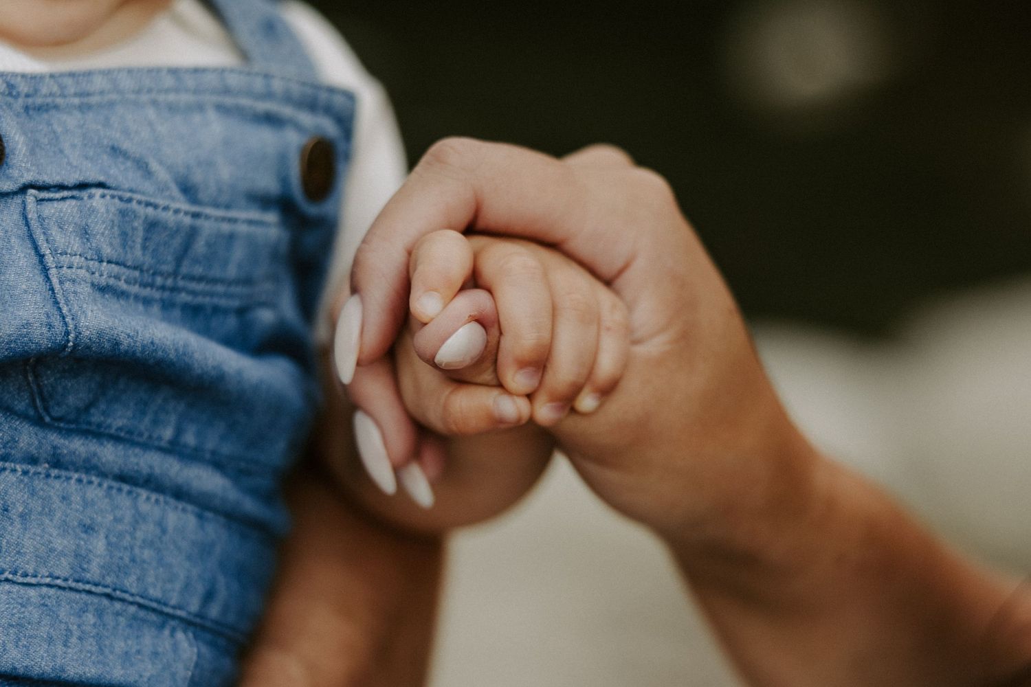 Two hands clasped together showing an engagement ring against denim clothing in a romantic moment.