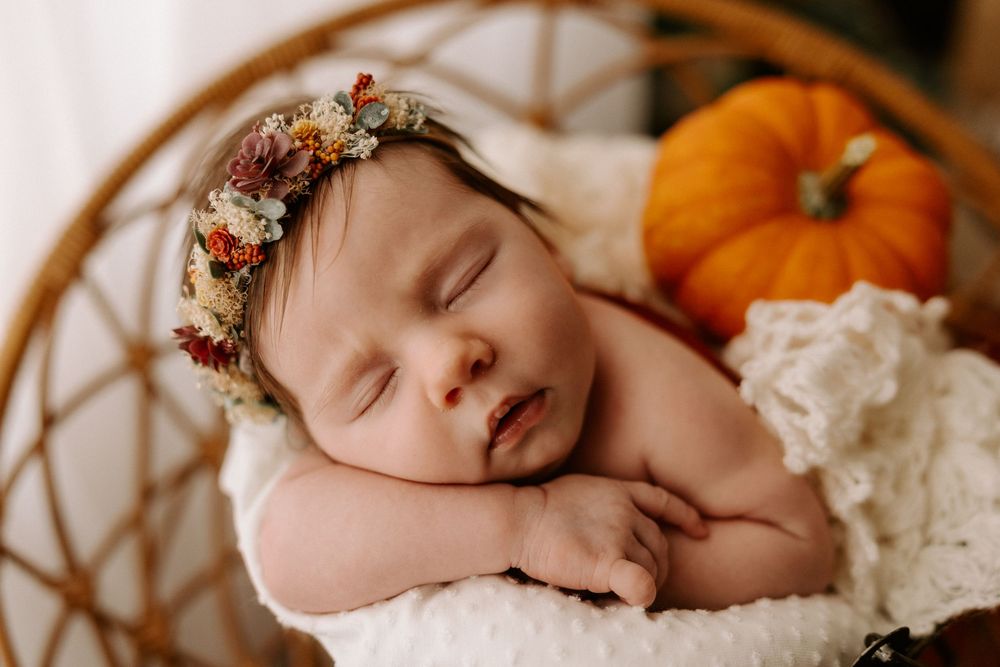 Peaceful sleeping newborn wearing delicate floral crown against soft cream backdrop.