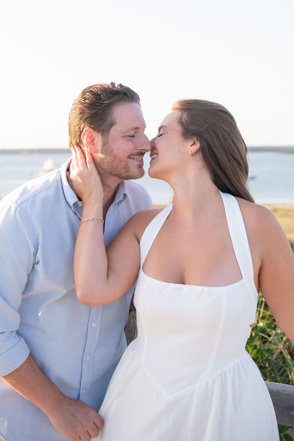 Romantic couple embraces on a sunny beach boardwalk during a golden hour photoshoot.