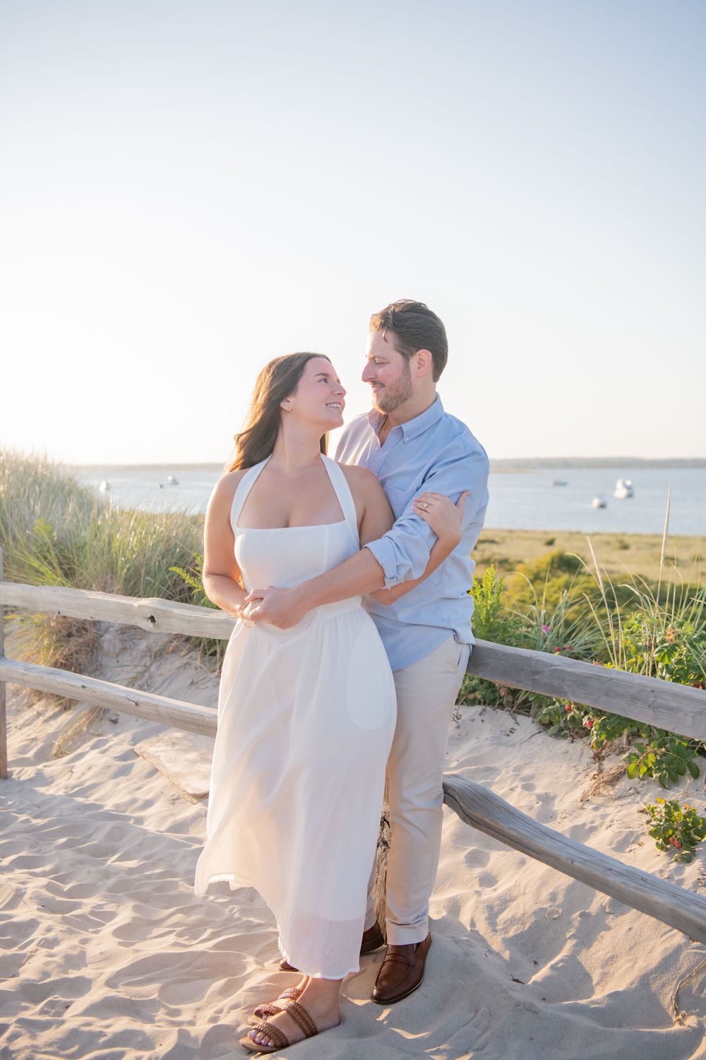 Loving couple poses together on coastal dunes with Rhode Island ocean views in the background.
