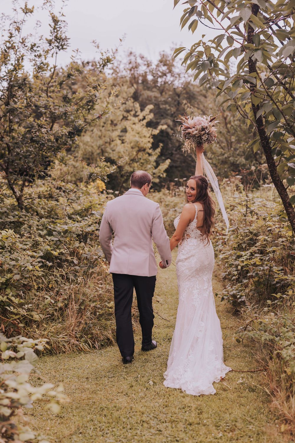 A couple in wedding attire walks hand in hand through an orchard on their special day.