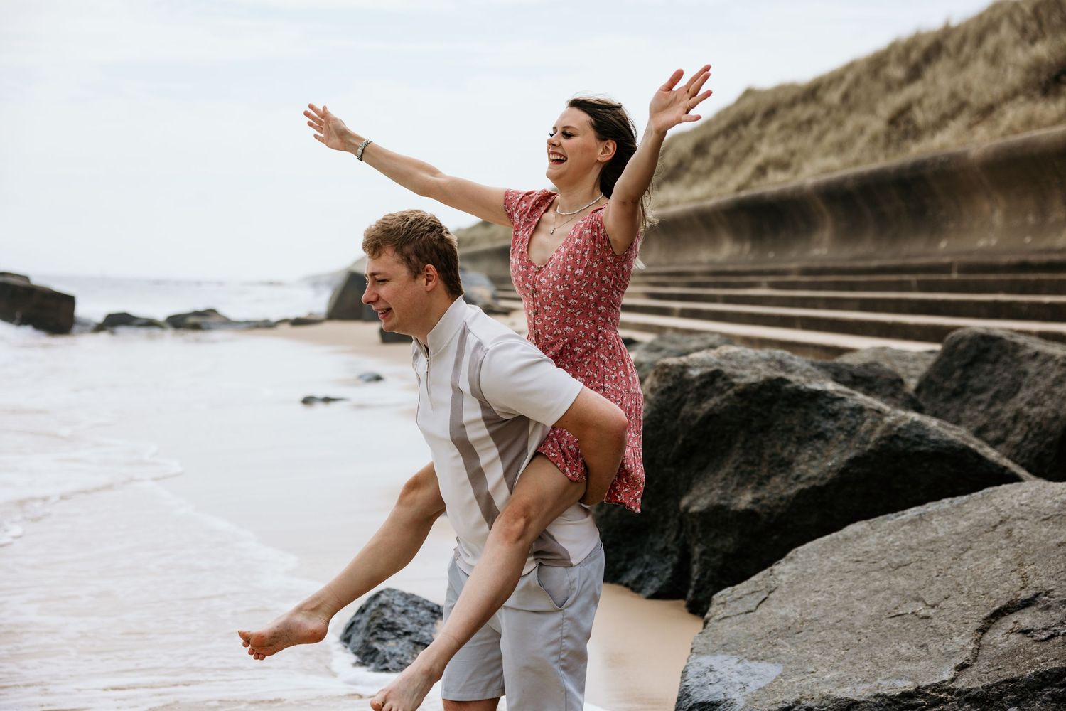 A couple sits on coastal rocks at the beach while enjoying a playful moment together during sunset.