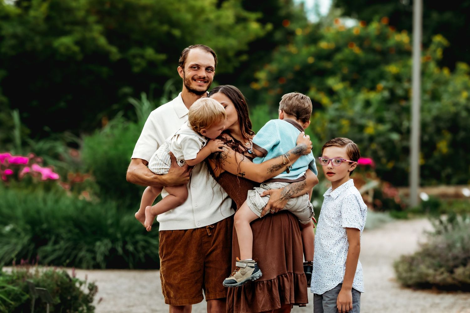 A family in brown and white outfits poses together in a garden setting during a professional photo session.