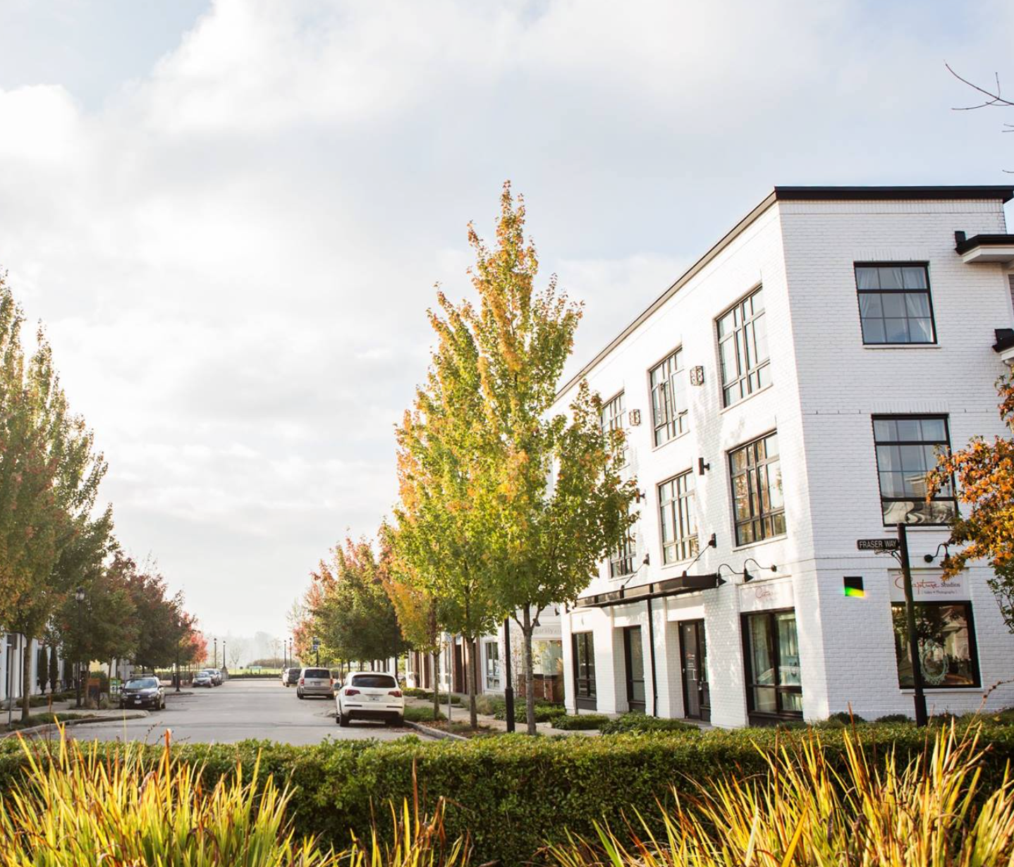 Modern white industrial buildings line a street with autumn trees and landscaping in a business park setting.