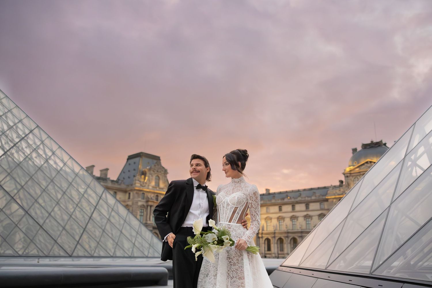 A couple in wedding attire shares an intimate moment on grand marble steps of a historic building.