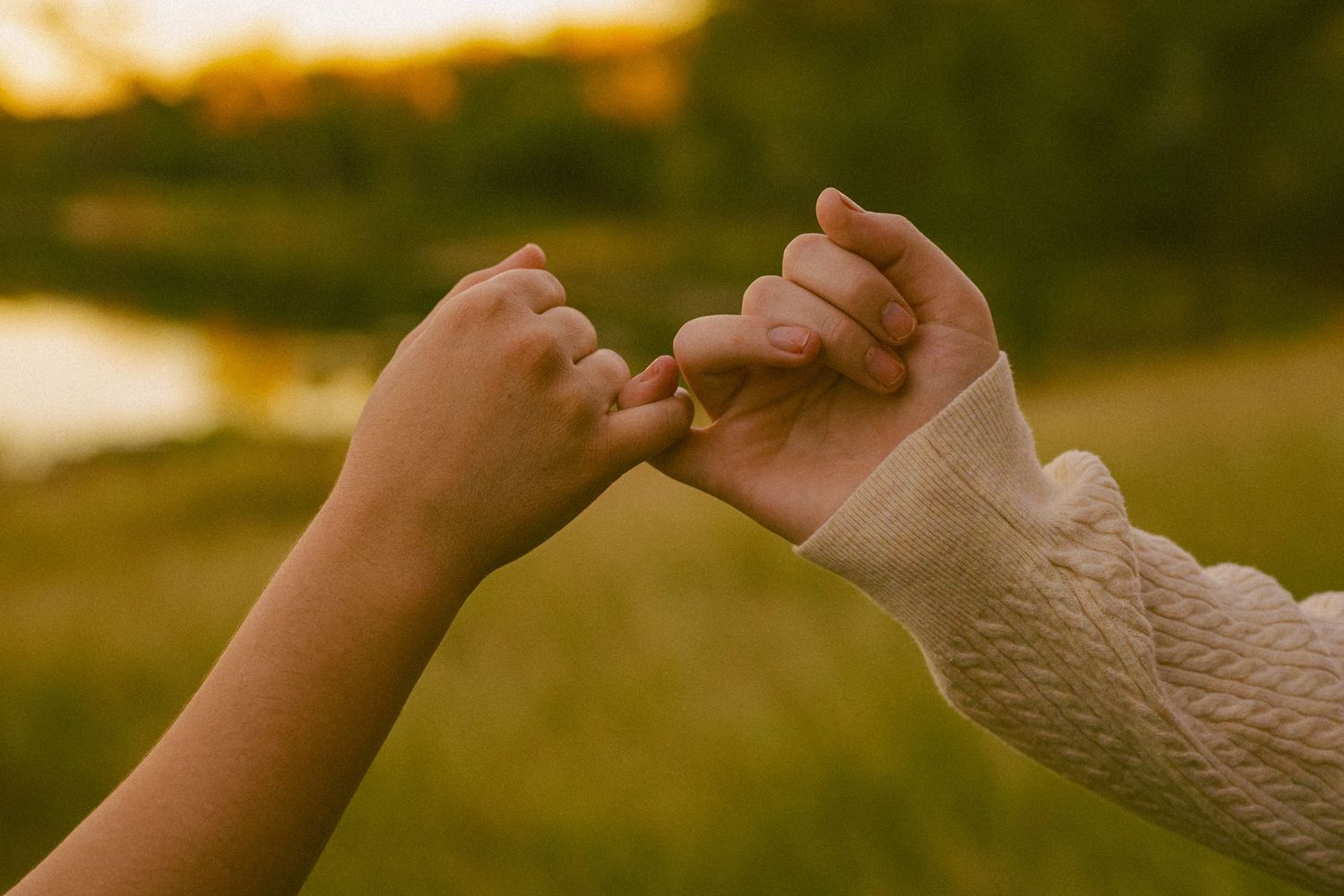 Two hands reach out and touch each other against a warm sunset background creating a silhouette effect. Pinky promise between best friends.