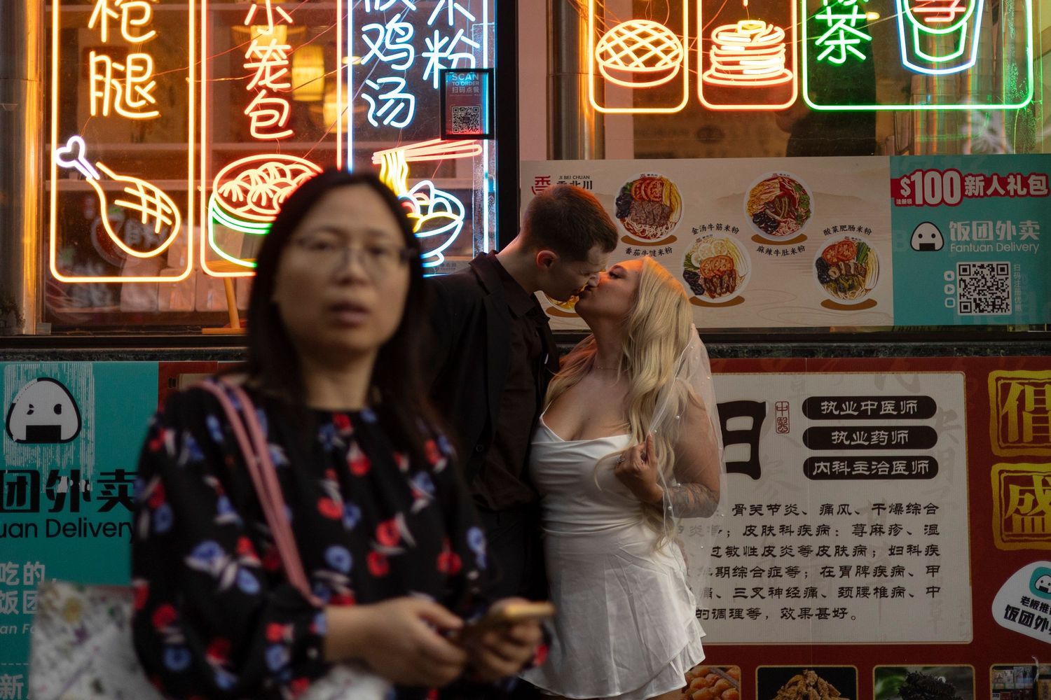 Colorful neon signs and menu displays illuminate the exterior of an Asian restaurant at night.