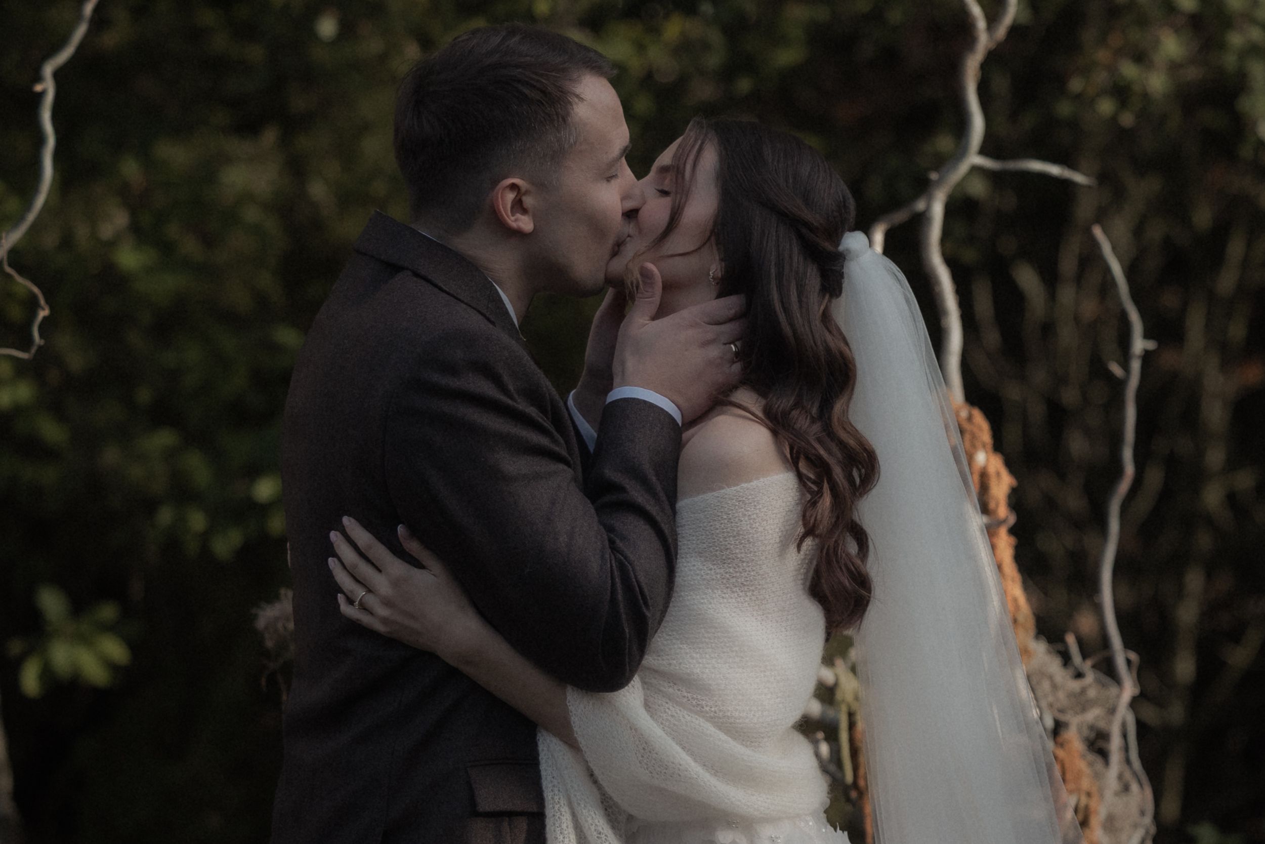 A romantic couple shares an intimate kiss during their outdoor wedding ceremony at sunset.