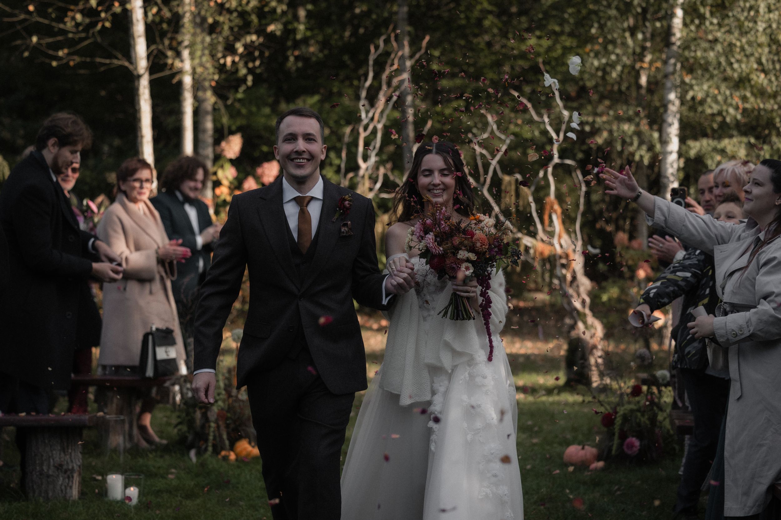 A joyful wedding celebration in a garden setting with guests clapping and cheering at sunset.