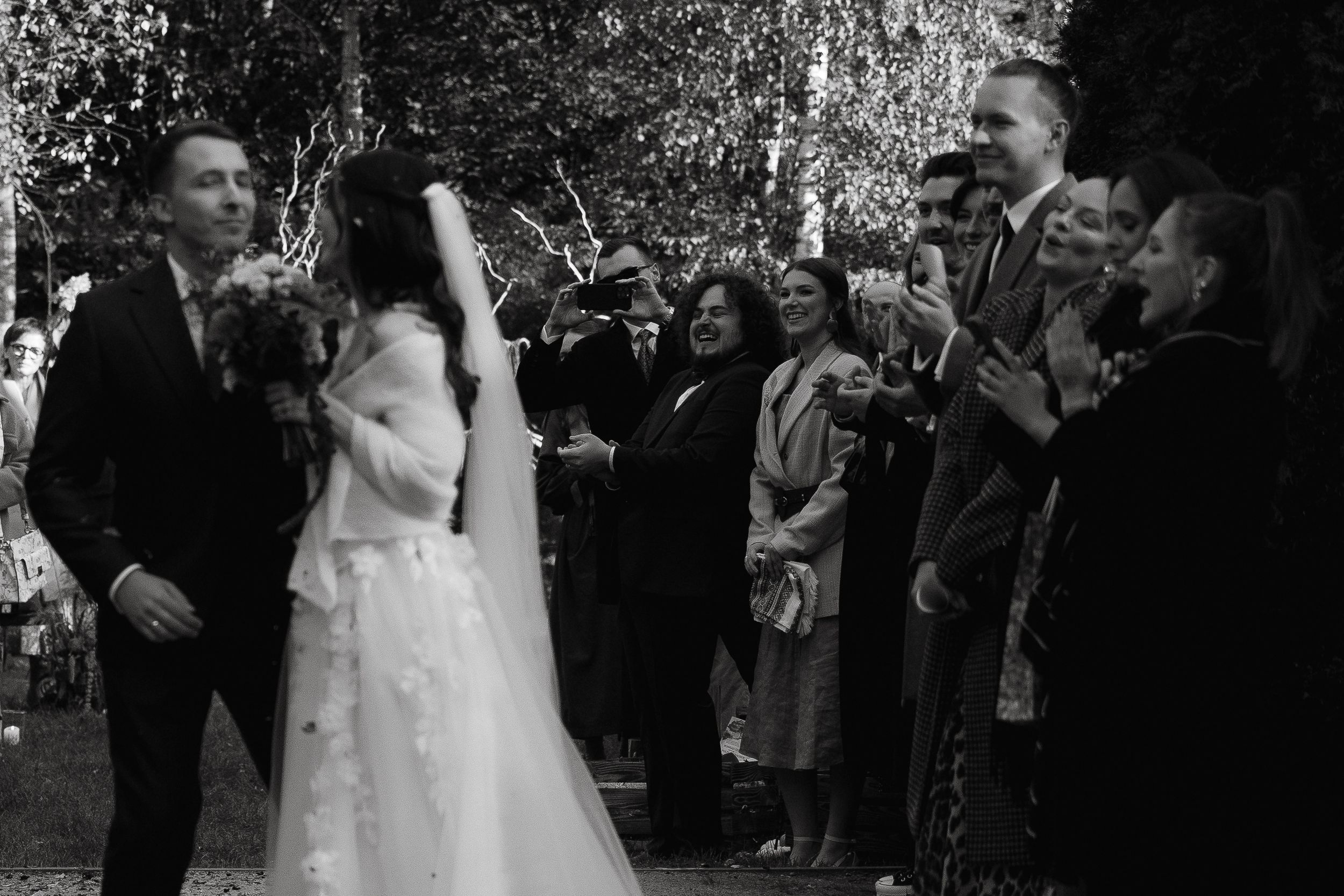 A wedding couple walks through a crowd of guests throwing flower petals and confetti during their outdoor celebration.