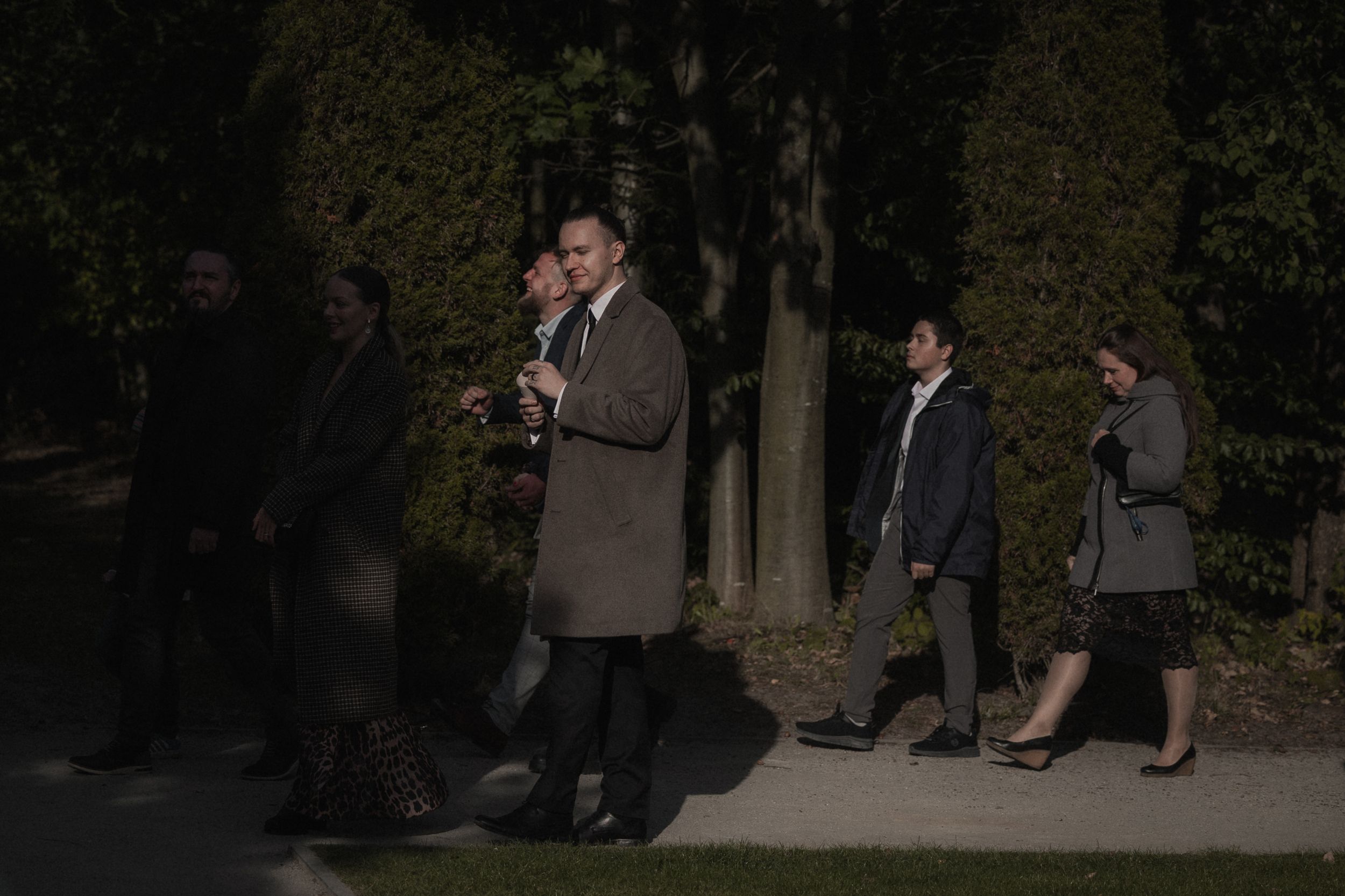 People walking along a dark path in a park at dusk with someone in a beige coat in the center.