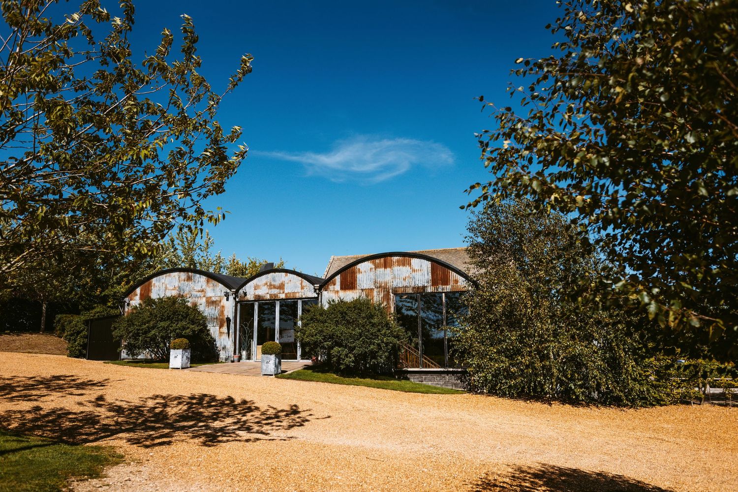 Panoramic view of a rural property with olive trees and buildings under a bright blue sky.