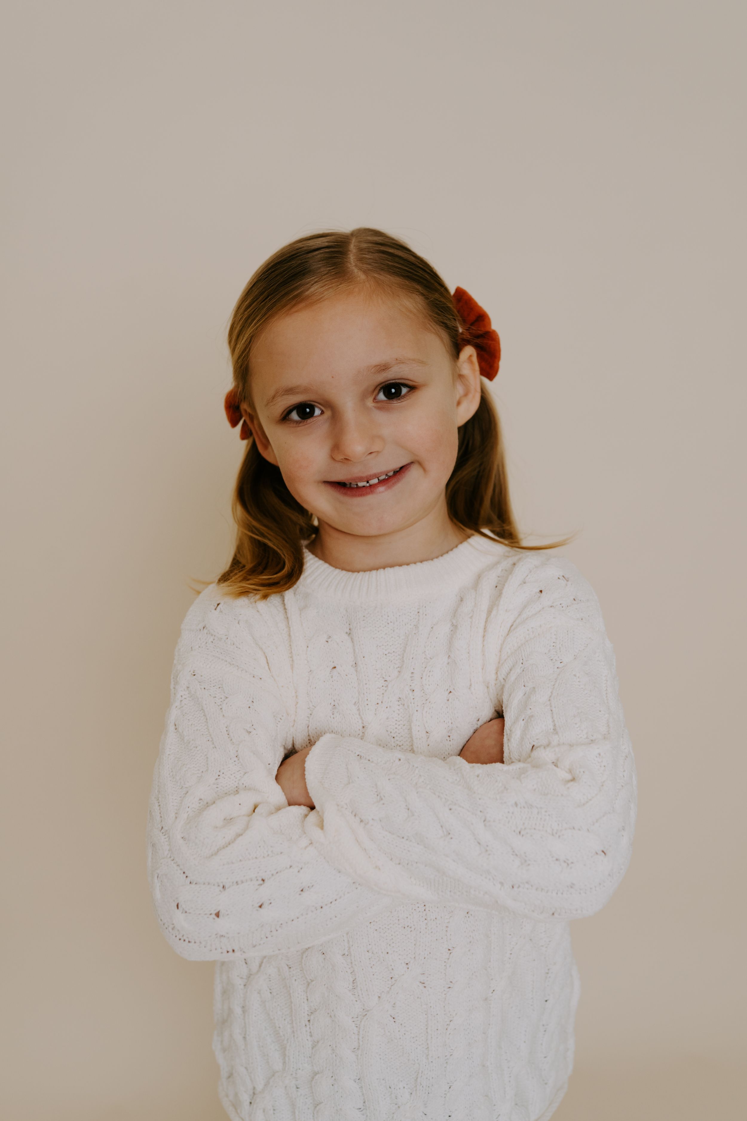 Person in white cable knit sweater posing with crossed arms against beige background.