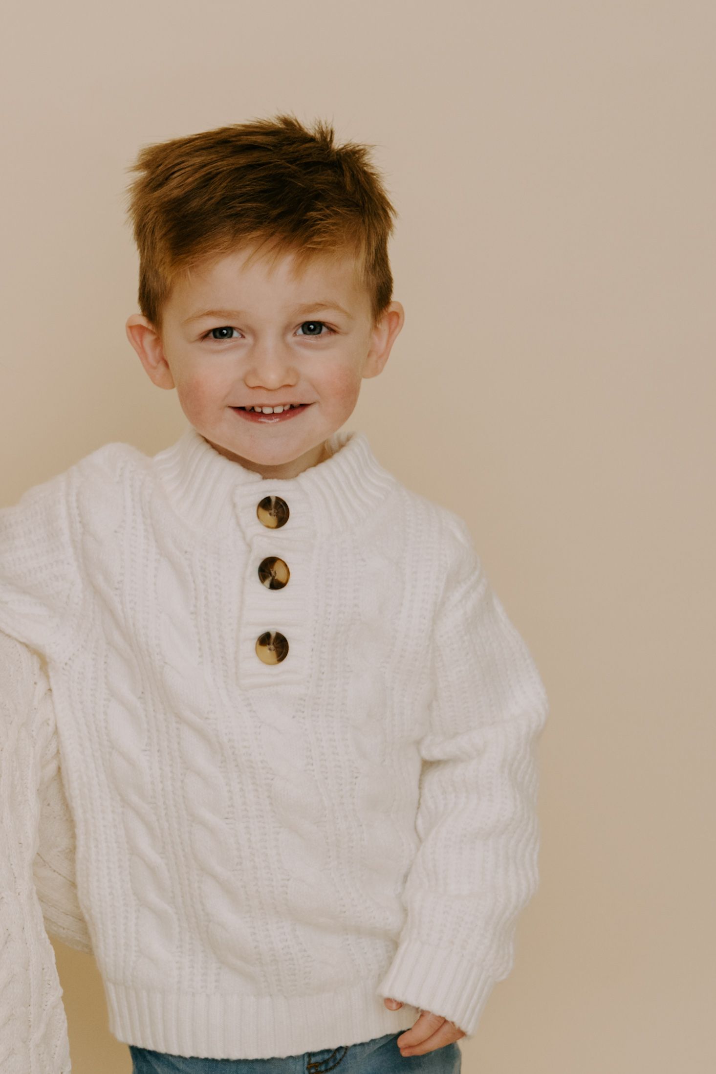 Child wearing white cable knit sweater with buttons smiling at camera.