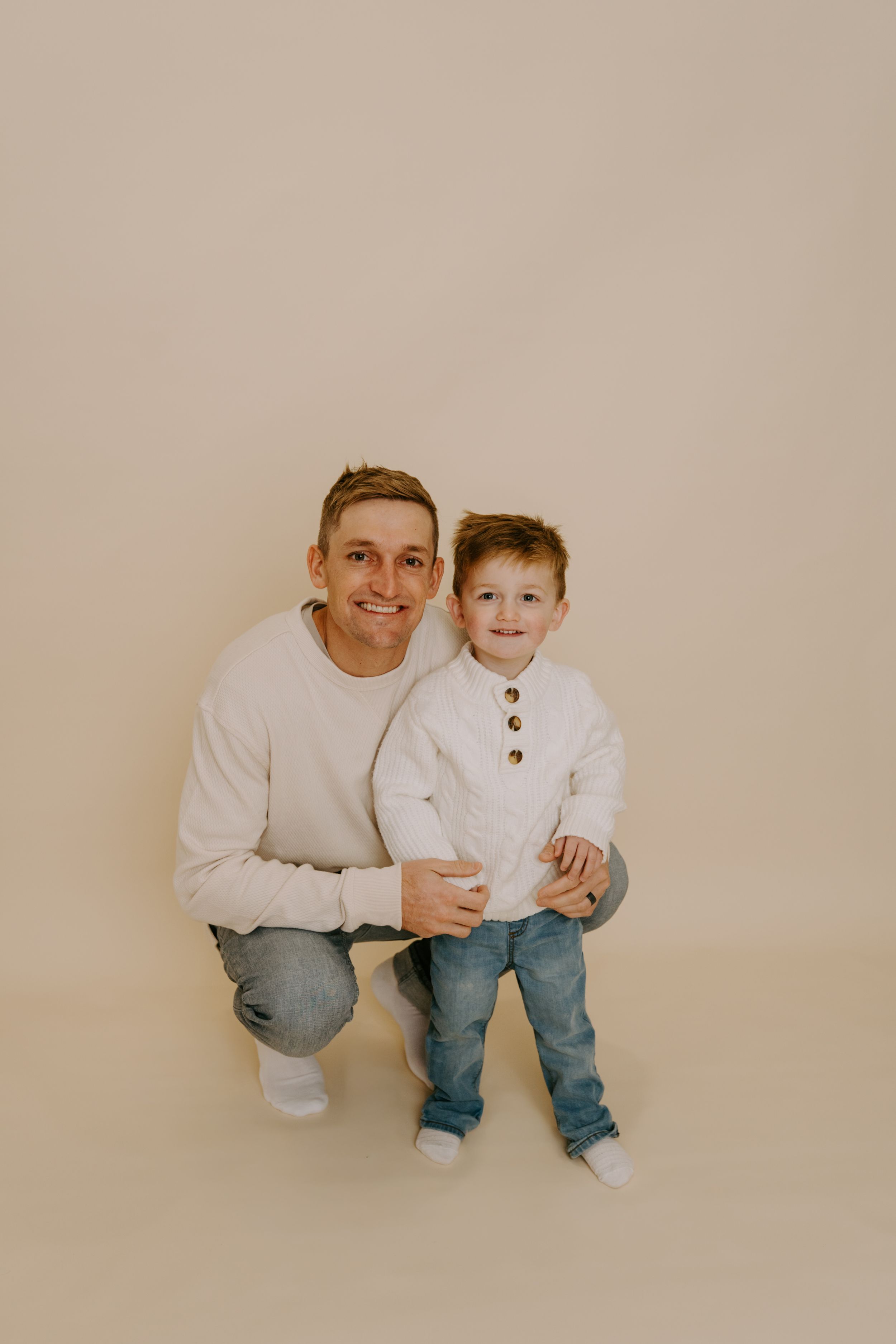 Parent and child wearing matching white sweaters pose together against neutral backdrop.