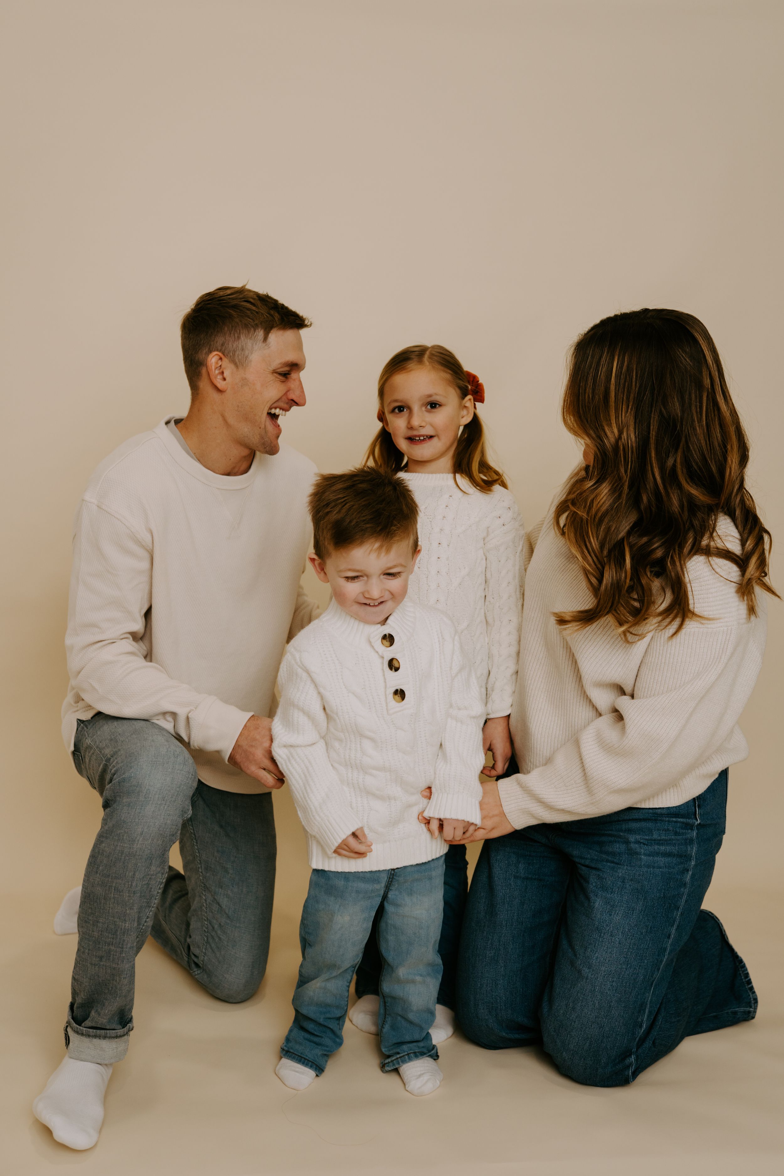 Happy family of four in matching white sweaters kneel together for portrait.