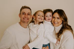 Family portrait with everyone wearing coordinated white sweaters against neutral backdrop.