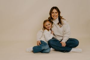 Parent and child in matching white sweaters sit together on beige background.