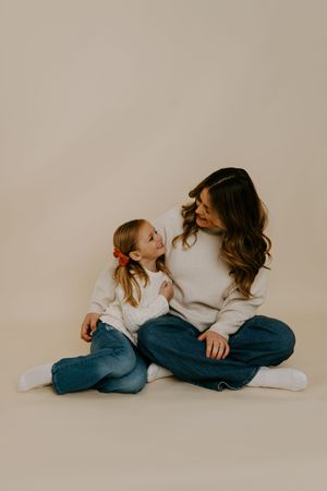Parent and child in cozy white sweaters share intimate moment on neutral backdrop.