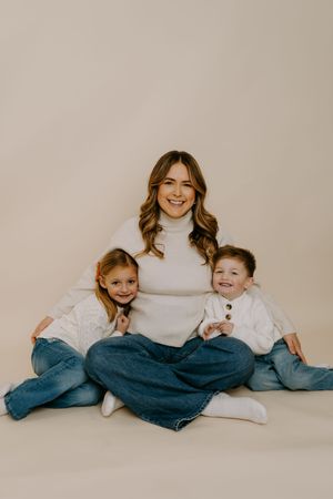 Family wearing coordinated white sweaters and jeans poses casually on beige background.