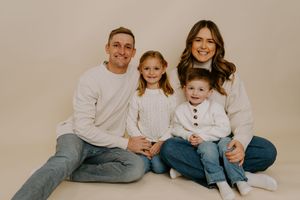 Family of four in matching white tops and denim sits together against neutral backdrop.