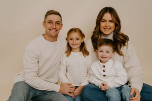 Casual family portrait with everyone wearing coordinated white sweaters and blue jeans.