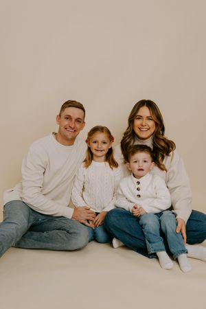 Family wearing coordinated outfits sits together on floor for studio photoshoot.
