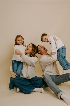A playful family photo session with coordinated white sweaters and jeans against a neutral backdrop.