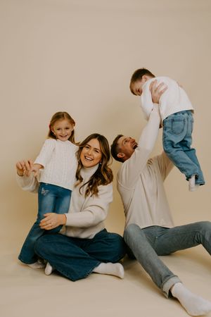 Candid moments of a family laughing together while wearing matching cream sweaters and denim.