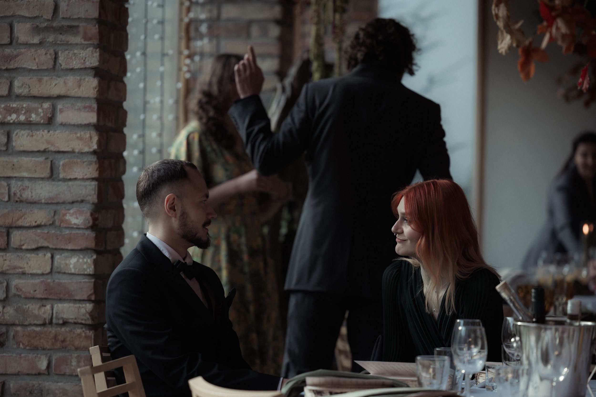 People gather at a dimly lit bar with exposed brick walls and industrial decor for drinks and conversation.