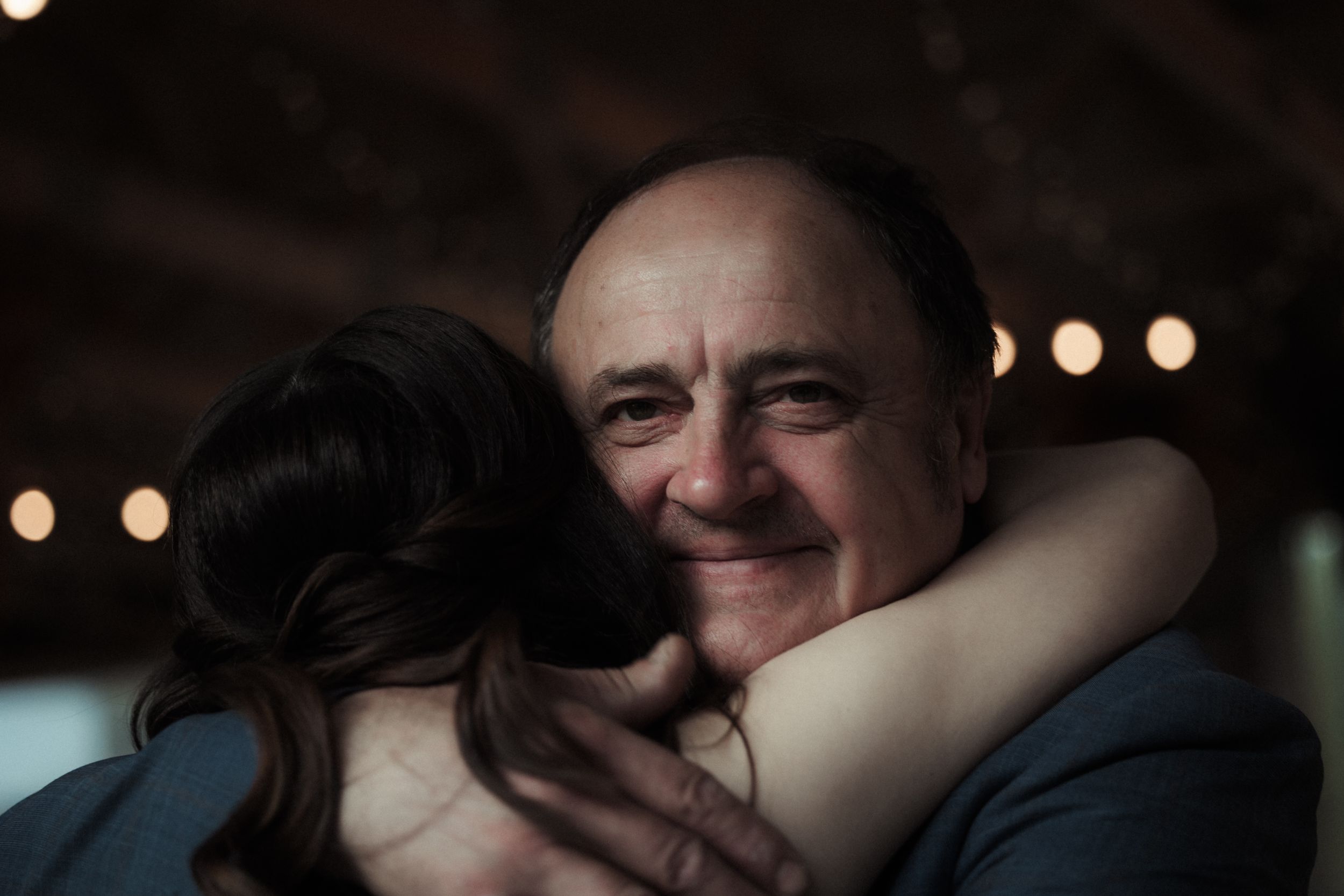 A couple shares a tender moment together in a dimly lit setting with bokeh lights in the background.