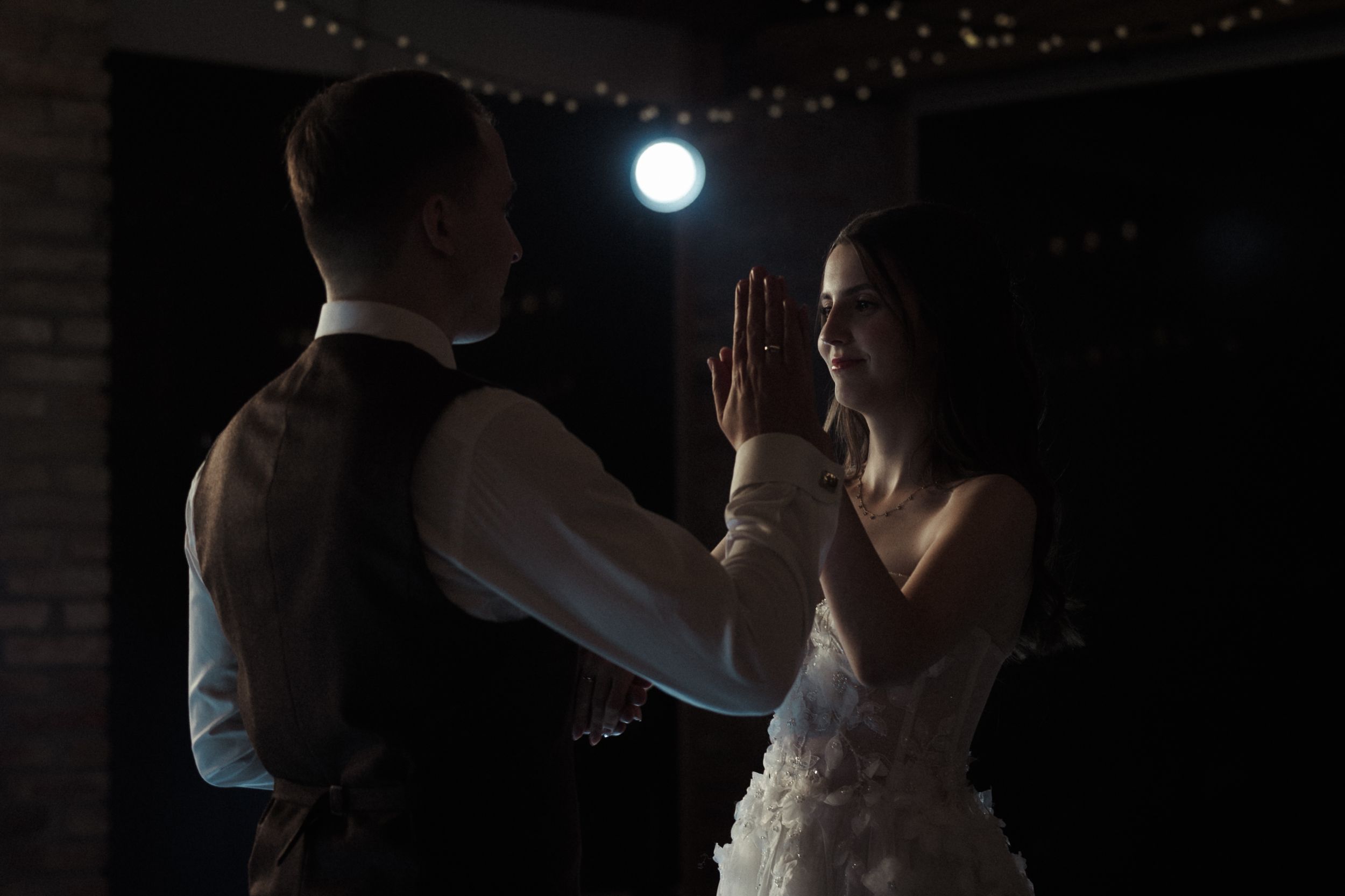 A silhouetted figure performs a dance move against a dark background with a bright circular light source.