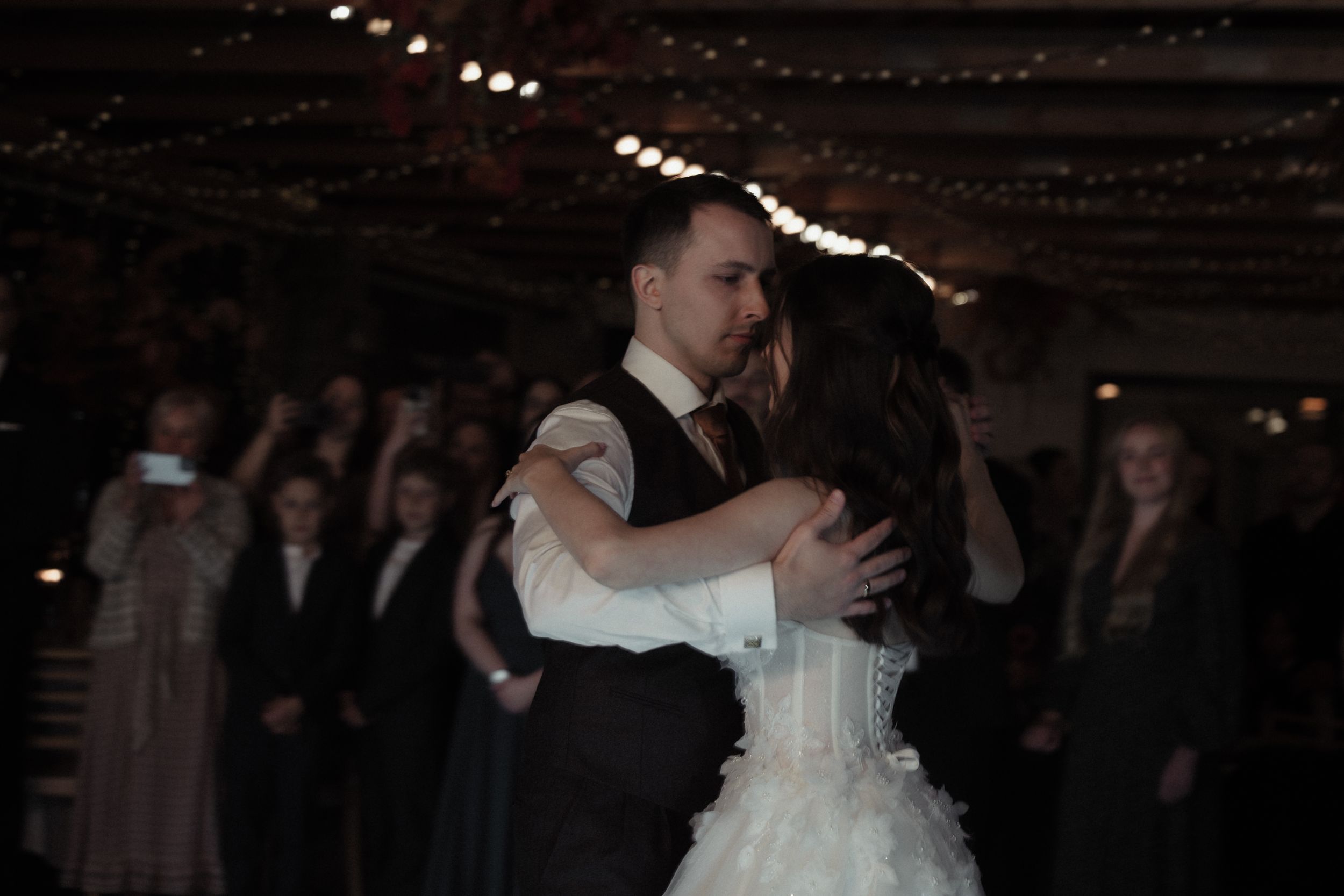 A couple shares a romantic dance at their wedding reception as guests look on from the dimly lit ballroom.