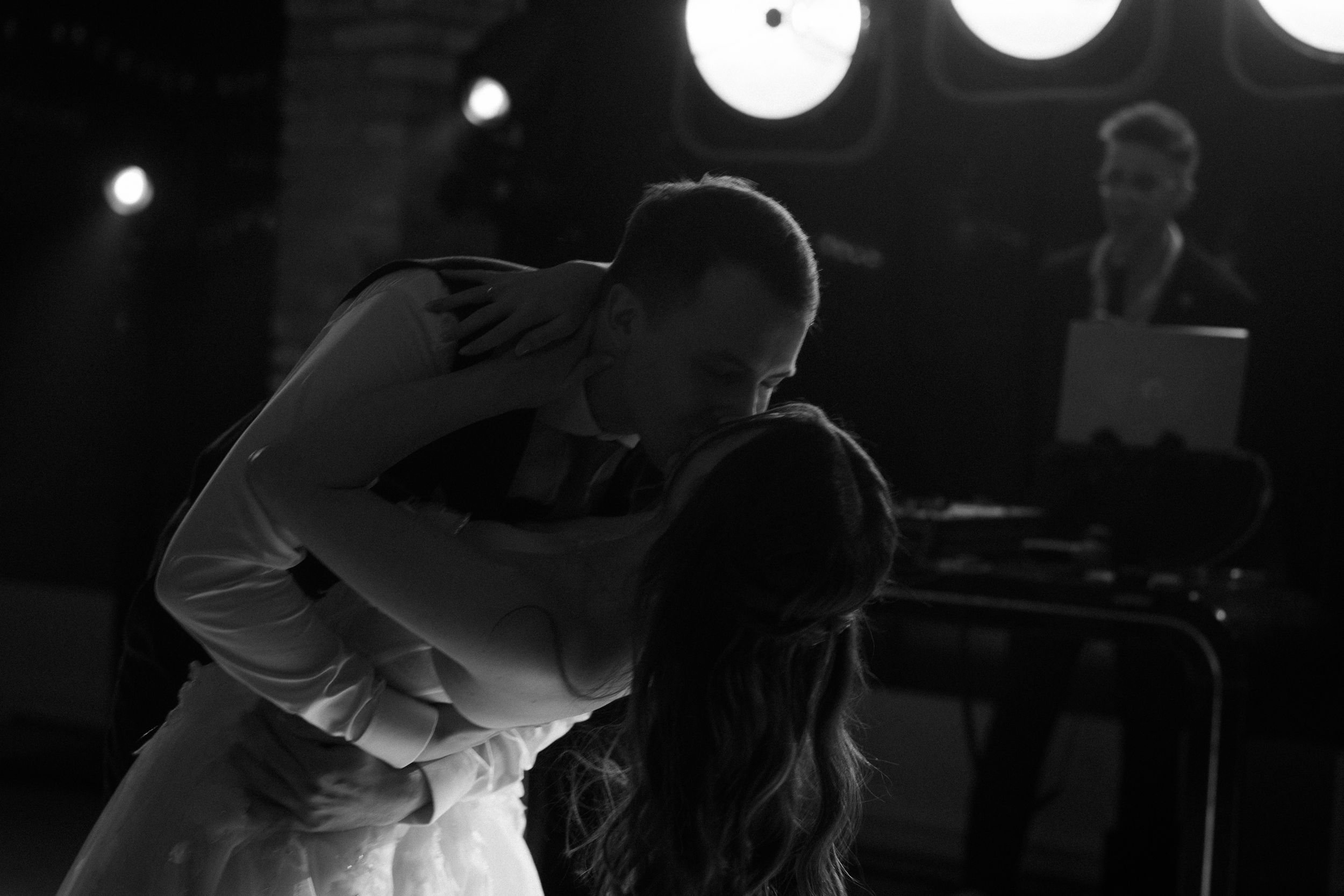A couple shares a romantic dance in black and white under dramatic lighting at an event.