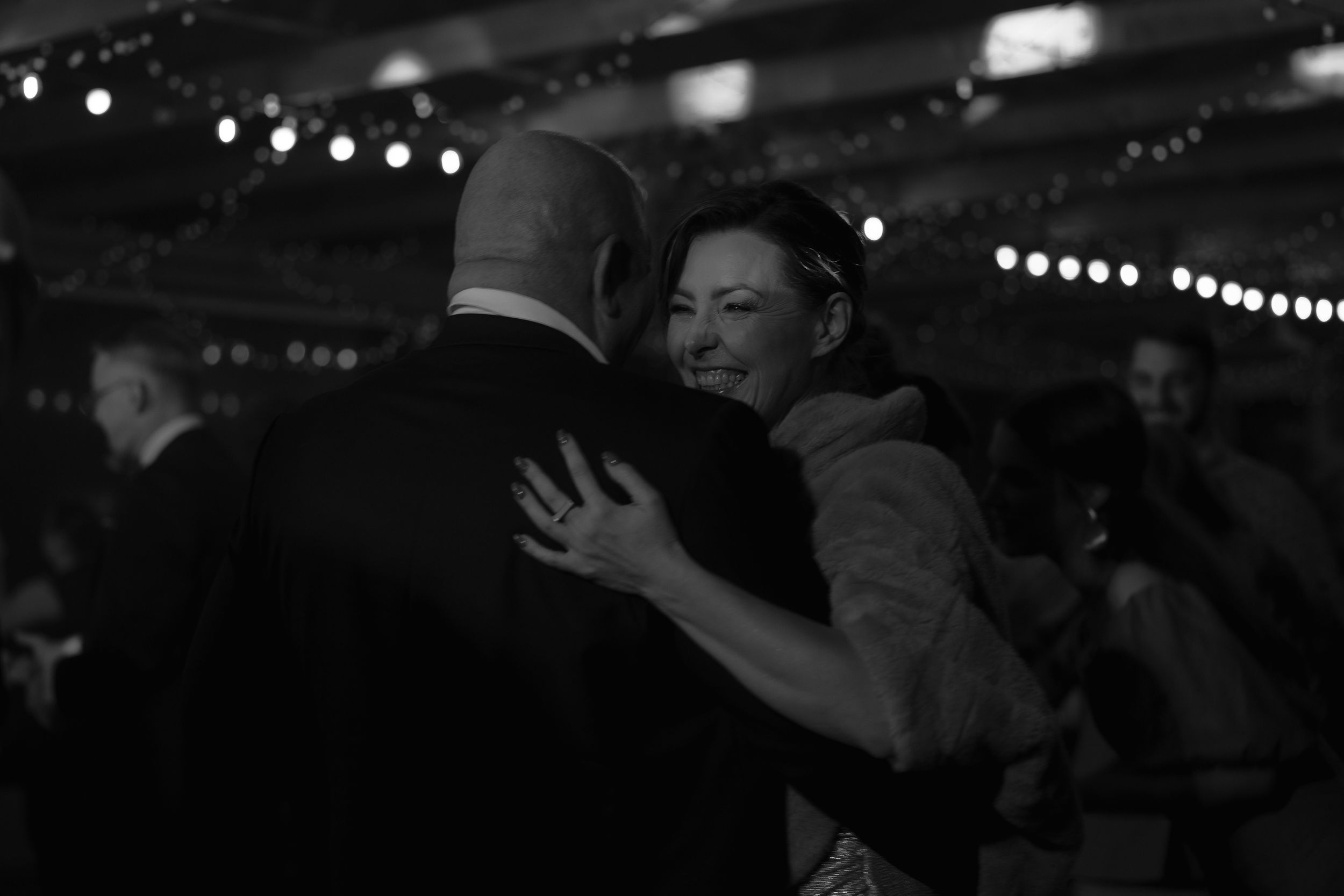 A black and white photo of two people embracing while dancing in a dimly lit venue with bokeh lights in background.
