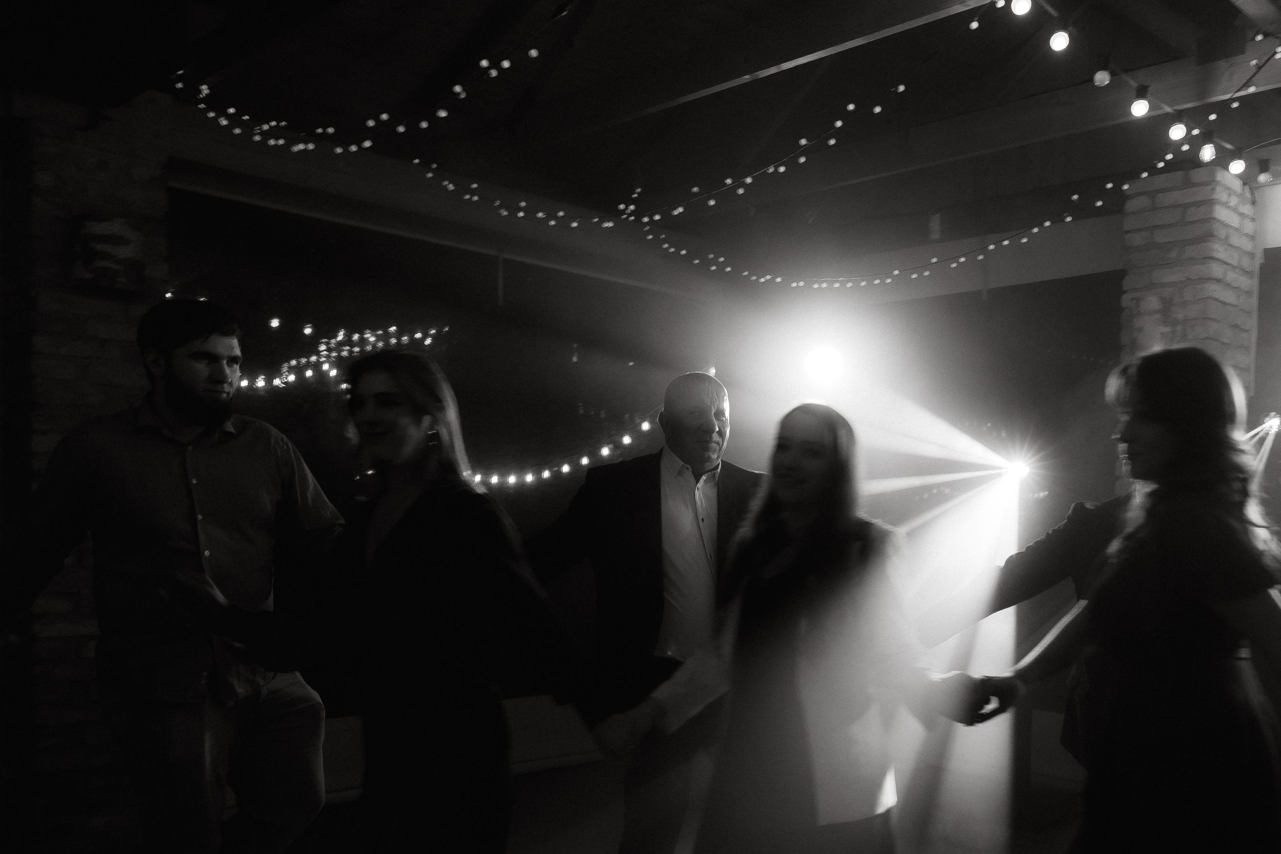 Silhouettes of people dancing and celebrating under string lights at a nighttime party or event.