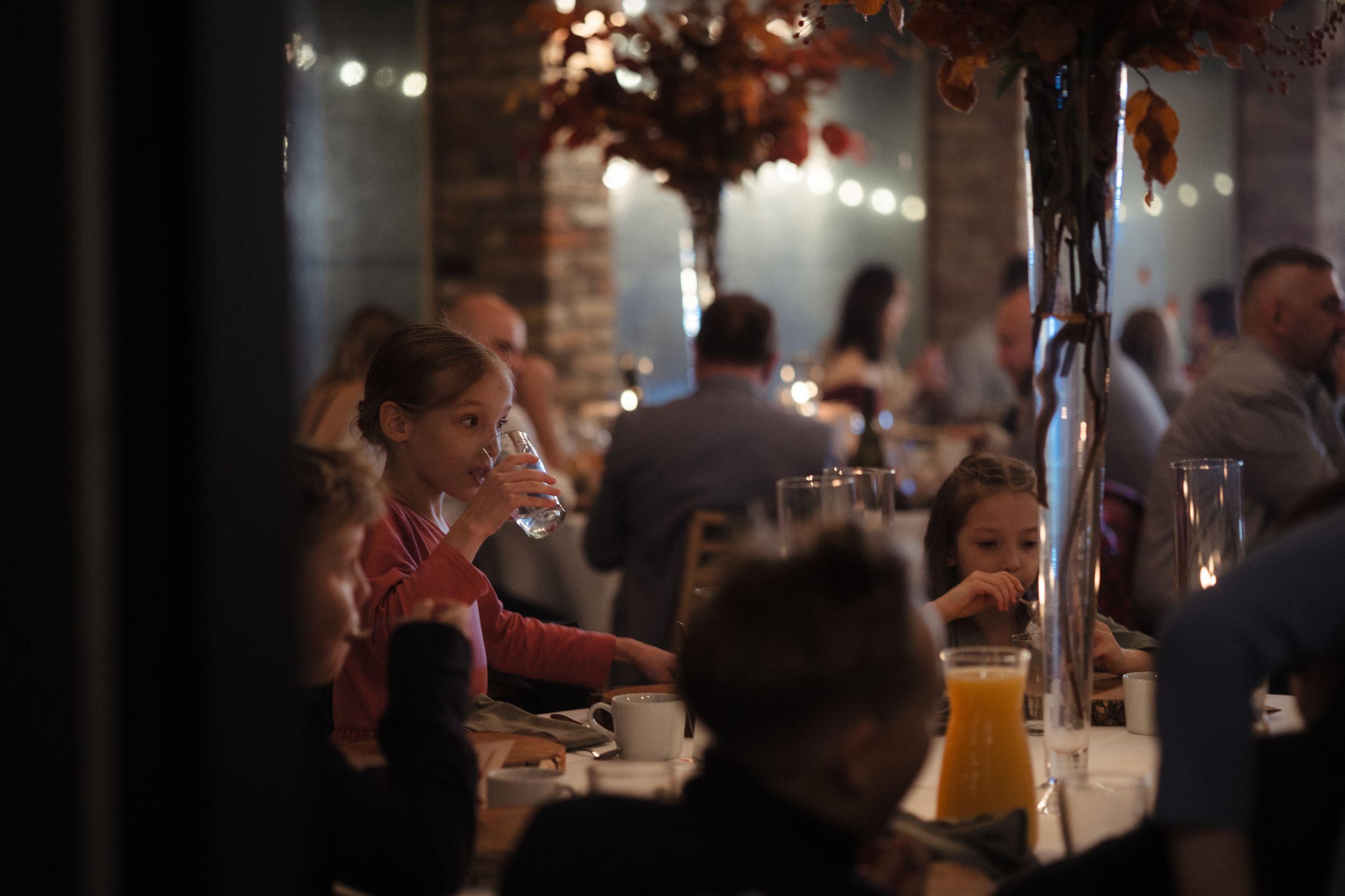 Guests enjoying a dimly lit evening celebration at a restaurant with warm ambient lighting and fall decor.