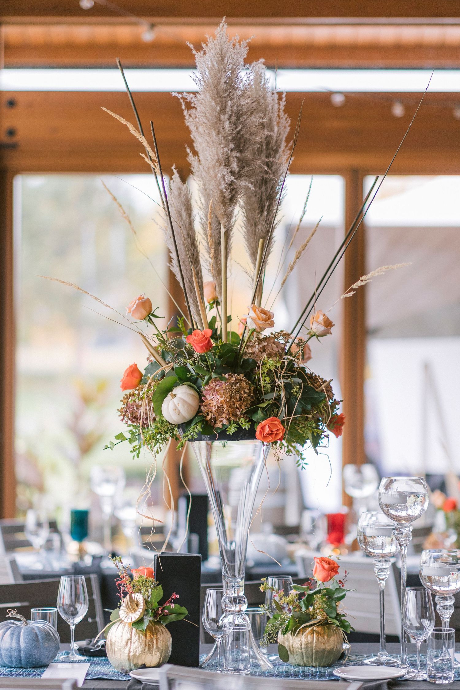 Elegant wedding reception table centerpieces featuring pampas grass, roses and greenery in metallic gold vases.