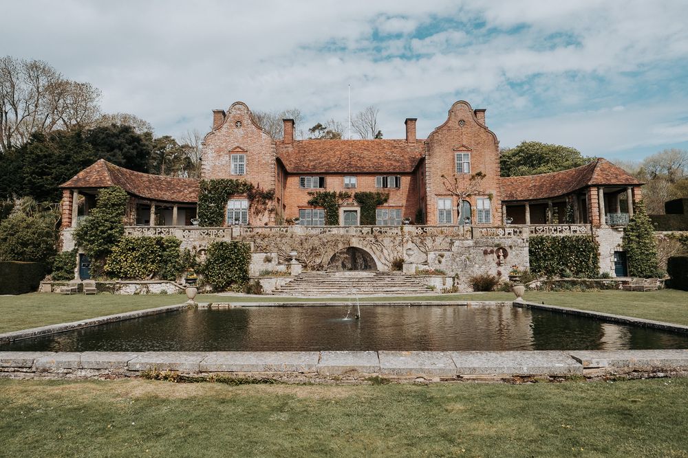 Panoramic view of a rustic stone mansion with multiple buildings and a reflecting pool in the garden landscape.
