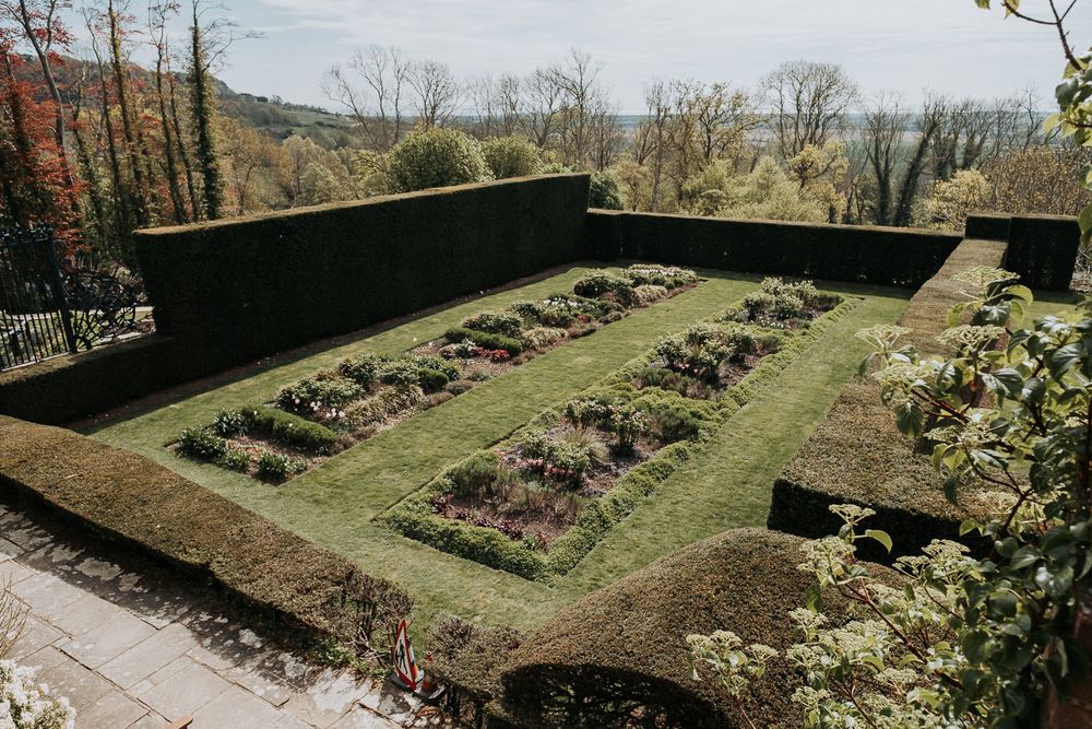 A formal garden with rectangular flower beds surrounded by tall stone walls in an autumn landscape.