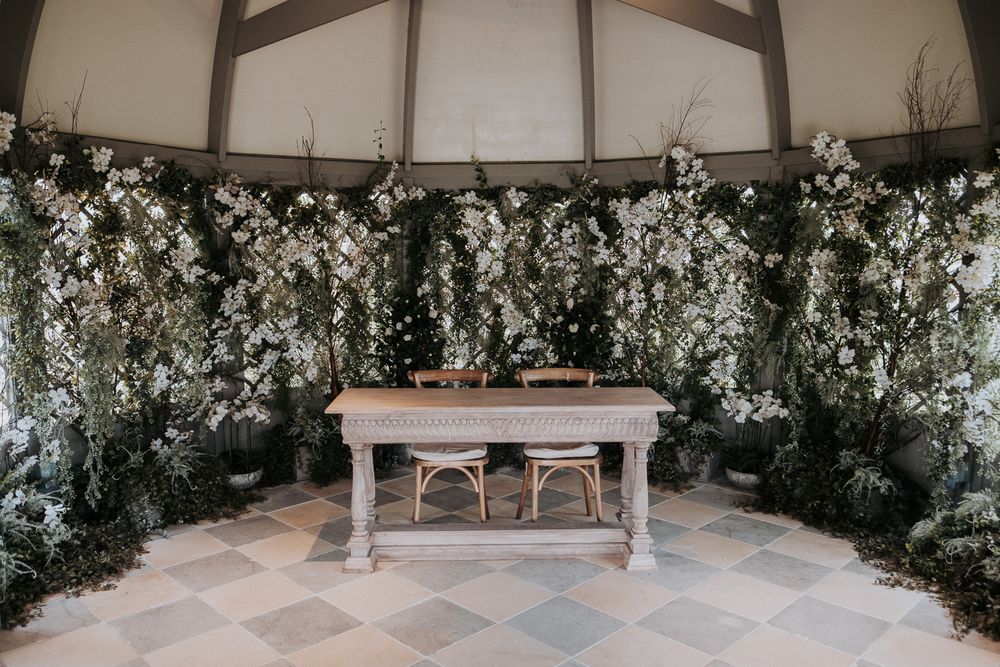 Elegant wedding venue interior with checkered floor and white floral arrangements along the perimeter.