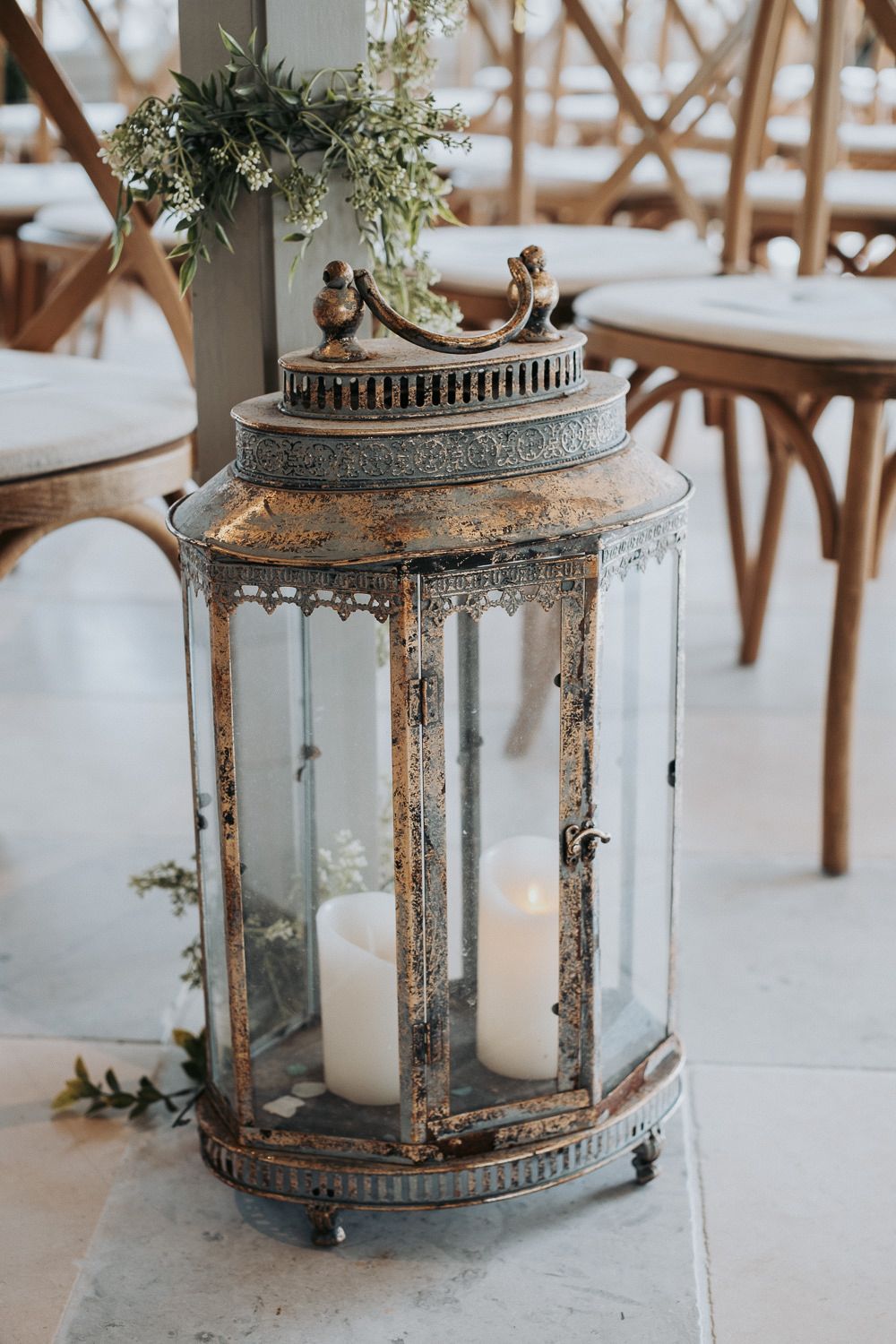 Vintage bronze lanterns with candles and greenery arranged as rustic wedding centerpieces.