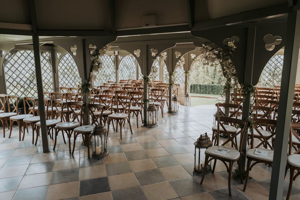 Elegant wedding venue with rustic cross-back chairs and checkerboard floors in a covered outdoor pavilion.